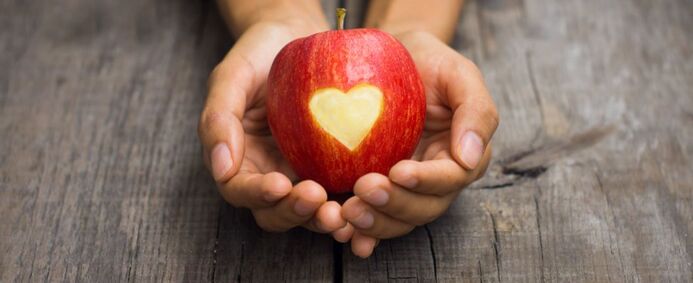 Hands holding an apple with a heart carved in it.
